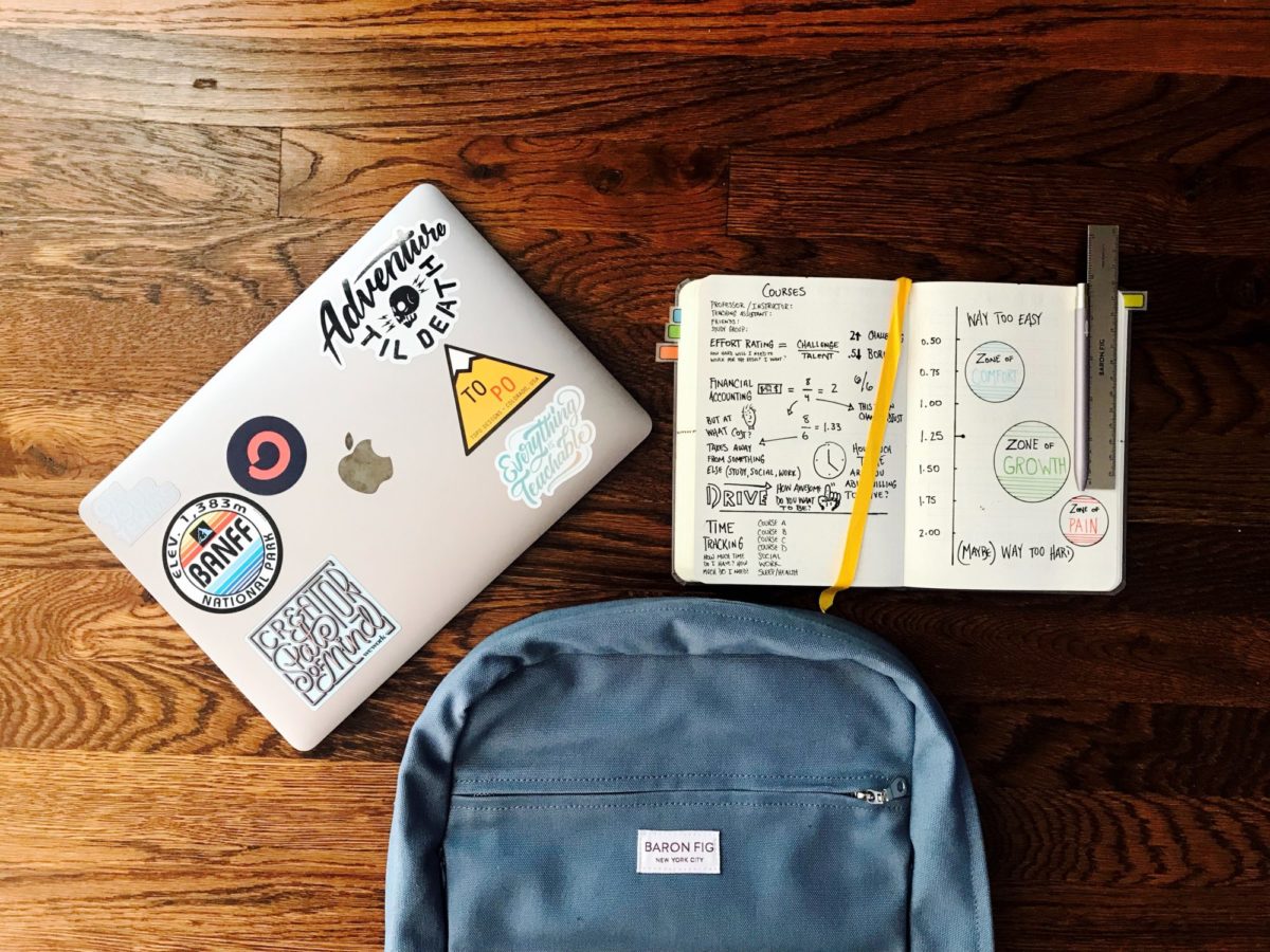 Laptop, Notizbuch und Rucksack liegen auf einem Holzboden